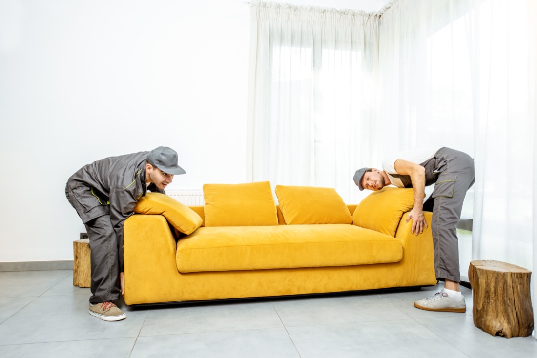 Two uniformed Elmer's movers setting a sofa down in a bright San Diego living room